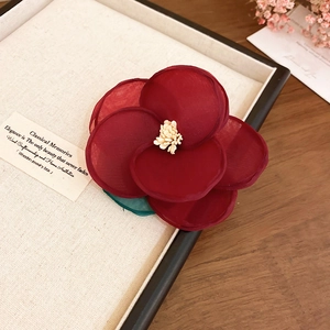 Close-up of a deep red fabric flower hair clip with yellow stamen on a cream jewelry tray