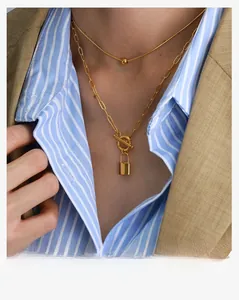 Close-up of double-layered gold paperclip chain necklace with a padlock pendant and OT buckle