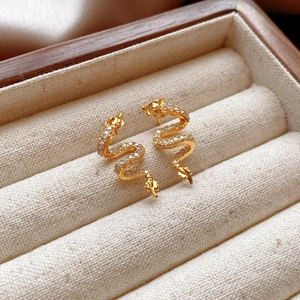 Close-up of golden dragon earrings with cubic zirconia in a wooden jewelry box