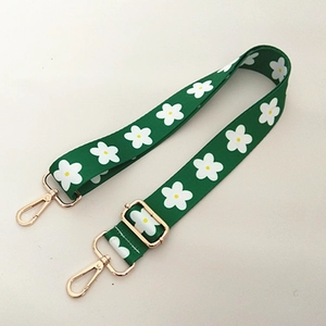 Close-up of green fabric bag strap with white flower patterns and gold metal buckles