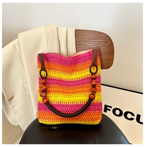 Detail of a rainbow straw tote bag featuring unique brown wooden bead handles on a chair