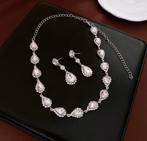 Detailed view of silver necklace and earrings set with clear teardrop crystals on black tray