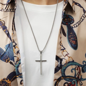 Close-up of a silver stainless steel cross pendant worn over a casual layered outfit