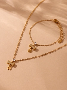 Detailweergave van gouden ketting en armband set met zirkonia bot en poot hangers