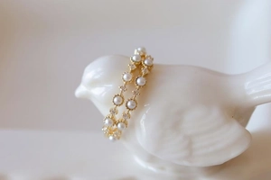 Close-up of a gold ring featuring delicate pearls and crystals on a white bird stand