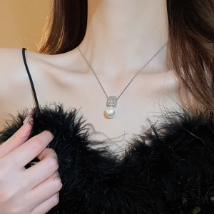Détail d'un pendentif carré en zircon et perle sur un mannequin avec fond de plumes noires