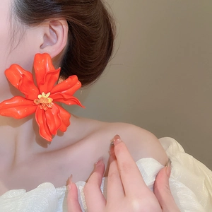 Close-up of model wearing vibrant oversized orange acrylic flower earrings for a vacation style