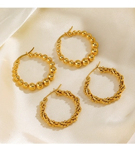 Détail de créoles dorées à perles et boucles d'oreilles torsadées sur du tissu de soie crème