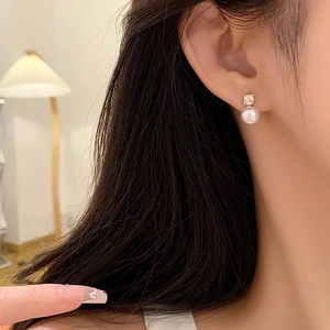 Close-up of elegant pearl stud earrings with sparkling zircon on a woman's ear