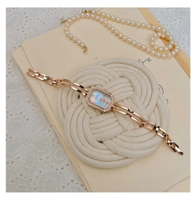 Close-up of rose gold square watch with mother-of-pearl dial on white lace and rope