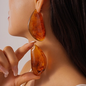 Détail de boucles d'oreilles géométriques en résine ambre avec texture et forme irrégulière