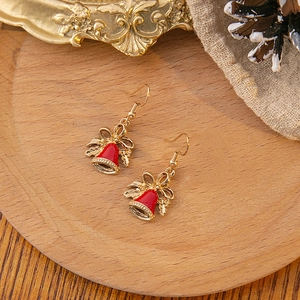 Detailed view of festive gold Christmas bell earrings with red enamel on rustic wood background