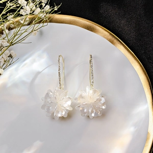 Detail shot of white shell flower earrings with gold tassels on elegant white ceramic plate