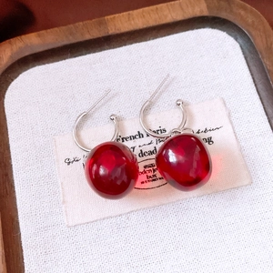 Macro view of cherry-shaped cherry drop earrings with translucent red beads on linen