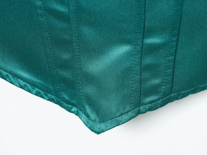 Dettaglio ravvicinato dell'orlo del corsetto in raso verde smeraldo con cuciture e tessuto lucido