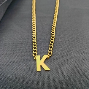 Macro view of golden Cuban link chain with a large capital letter K pendant on grey fabric