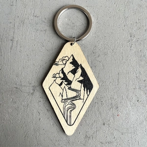 Macro shot of a diamond-shaped wooden keychain featuring a vintage mountain carving
