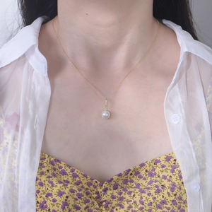Close-up of elegant gold chain necklace with round white pearl and sparkling zircon pendant