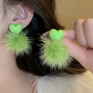Detail of a model wearing green heart plush pom-pom earrings with soft resin finish
