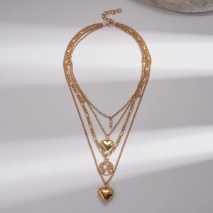 Gold multi-layer necklace with heart and world map pendants over a white shadow background