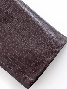 Close-up detail of dark brown faux crocodile skin texture on shiny autumn jacket fabric