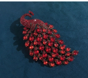 Macro shot of detailed peacock brooch with deep red rhinestones and dark alloy base