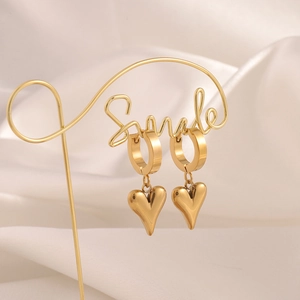 Detail of gold 3D heart dangle earrings on a gold stand against white silk background