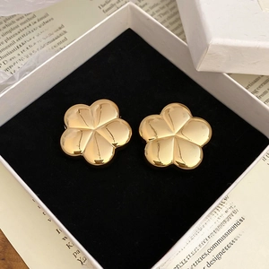 Detailed view of polished golden flower stud earrings resting on a black velvet gift box