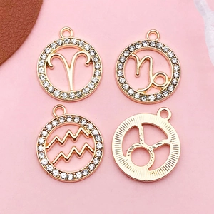 Golden alloy zodiac pendants with white rhinestones on a pink background