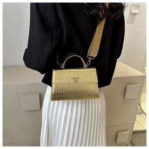 Detail of gold crocodile pattern handbag with turn-lock clasp and wide fabric strap