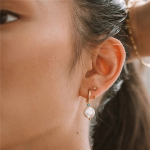 Close-up of gold star stud and hoop earring with pearl and turquoise on model's ear