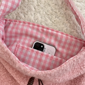Detalle de bolso rosa de peluche con forro de cuadros y bolsillo para móvil