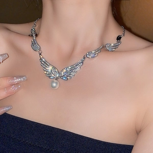 Close-up of sparkling winged pendant with a round pearl charm on model's neck