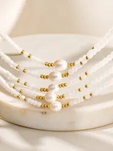 Detail of beaded necklace with central oval pearl and golden spacers in layered display