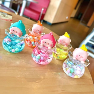 Five assorted acrylic liquid sand pig charms on a wooden surface in warm lighting