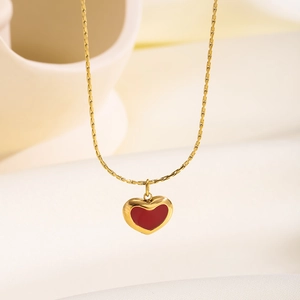 Gold titanium steel necklace with a vibrant red heart pendant on a soft cream fabric