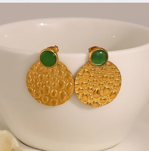 Macro shot of gold hammered metal earrings featuring a vibrant green gemstone detail