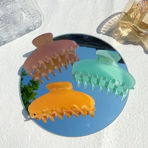 Close-up of three colorful matte hair claws in pink, green, and orange on a mirror