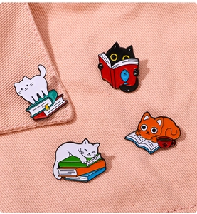 Detailed close-up of cute enamel cat pins reading books on pink textured fabric background
