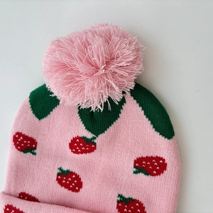 Pink knit hat with strawberry jacquard pattern and large fluffy pompom for autumn winter