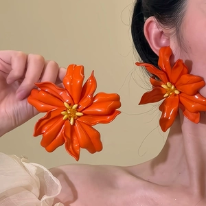 Handheld view of large orange acrylic flower earrings with yellow centers on beige background