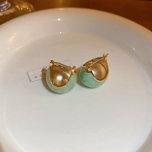 Close-up of green drip oil heart C-shaped earrings on a white ceramic plate