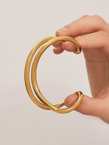 Dettaglio di un bracciale rigido aperto minimalista a doppio strato in acciaio dorato