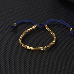 Detailed close-up of navy blue braided cord and irregular golden metal beads on bracelet