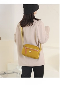 Close-up of mustard yellow nylon crossbody bag with adjustable strap and golden zippers
