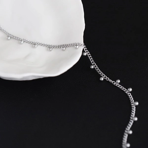 Macro detail of polished silver bead chain and elegant silver links on a ceramic tray