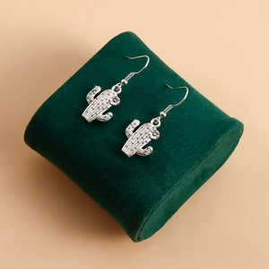 Détail des boucles d'oreilles cactus argentées avec textures florales sur support vert