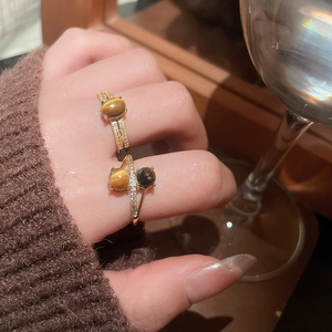 Detailed view of gold plated tiger eye rings worn with stylish brown knitwear and glass