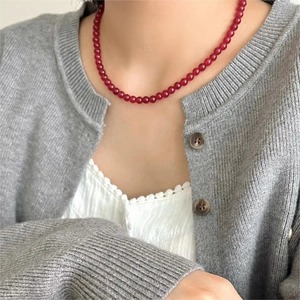 Detail of red agate bead necklace on model wearing a grey cardigan and lace top