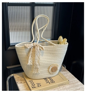 Detail of hand-woven cream tote bag with lace bow and daisy embroidery on marble